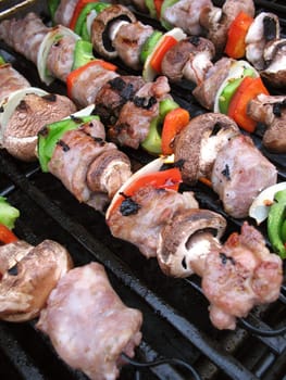 Sausage shish kebabs on skewers, cooking on the grill.  Shallow depth of field.