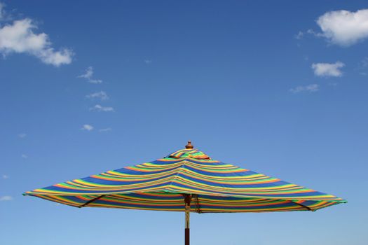 A rainbow-striped beach umbrella over a clear blue sky.