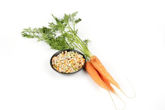 Bunch of ripe crunchy carrots and soup pulses in a small black dish on a reflective white background