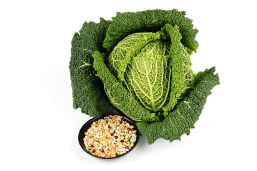 Single fresh ripe green cabbage and soup pulses in a small black dish on a reflective white background 