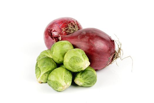 Two raw unpeeled red onions with a small pile of green sprouts on a reflective white backgrounds