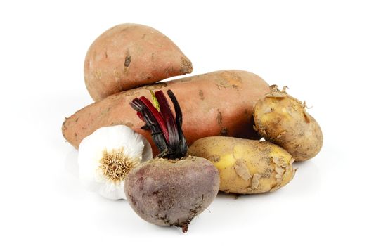 Two raw unpeeled sweet potatoes with garlic, brown potatoes and beetroot on a reflective white background