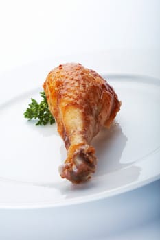 Closeup picture of roasted chicken leg on the white plate.