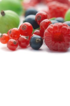 Spilled  mixed berries on white background whith a raspberry  in the foreground in focus.