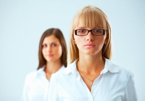 Two young  serious business women on light blue background whith a fair hair woman in focus