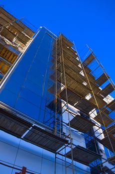 facade of the modern building with blue window with scaffolding on background blue sky