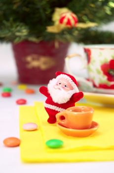 lucky small santa claus with cup of tea and sweetmeat on background fir tree