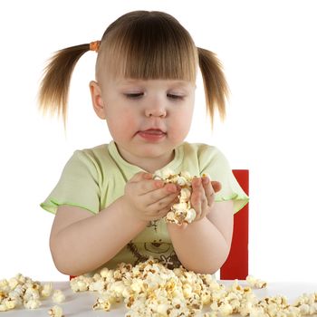 little girl on white background  sits at the table, keeps in hand popcorn and looks at it