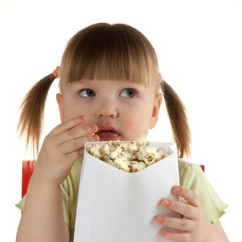 little girl on white background  eats popcorn in white paper package and looks to the right