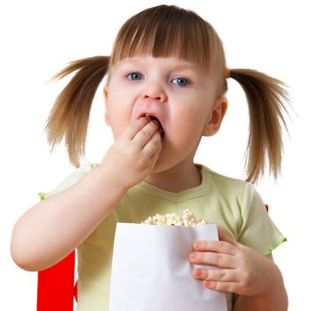 little girl sits on chair, keeps package with popcorn and eats