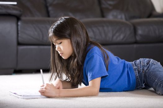 Little girl doing her homework, lying down on floor