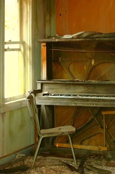 Ancient piano sits in abandoned, decaying old building with chair in place, as if the last player left suddenly and never returned.