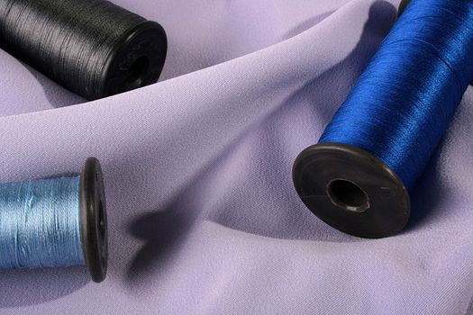 Coils with dark blue, black and blue threads against a lilac fabric.