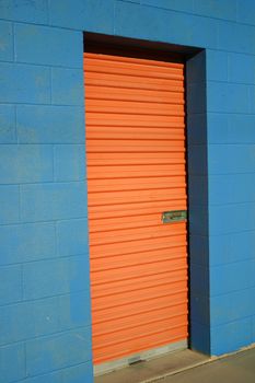 Bright orange door to storage unit in bright blue building