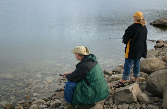 Man and woman are fishing for trout in the beautiful blue waters of Twin Lakes in the mountains of Colorado on a chilly spring day.