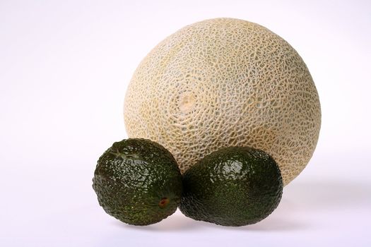 Ripe melon and two green avocados on a white background.