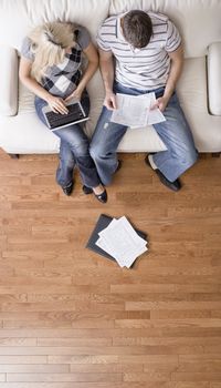 High angle view of young couple sitting on a couch with a laptop and paperwork. Vertical shot.