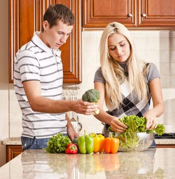 Young couple in kitchen make salad with fresh vegetables. Square shot.