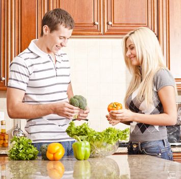Young couple in the kitchen have fun while making a fresh salad. Square shot.