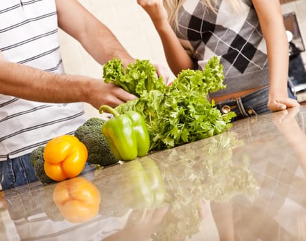 Cropped view of a young couple stand behind a kitchen counter full of vegetables. Horizontal shot.