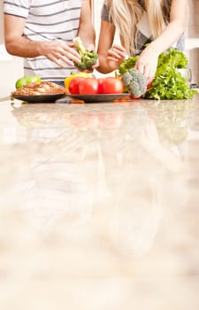Young couple picks through fresh vegetables at the far end of a kitchen counter. Vertical shot.