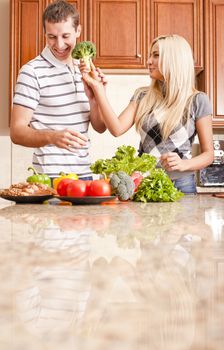 Young couple in a kitchen joke around with fresh vegetables. Vertical shot