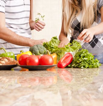 Young couple pick through fresh vegetables behind a kitchen counter. Square shot.