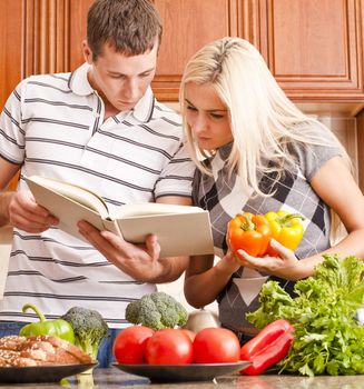 Young couple look at a recipe book in the kitchen. The counter is full of fresh vegetables. Square shot.