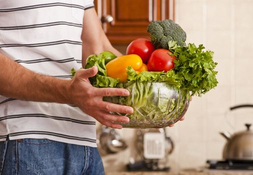 Man in striped shirt holding a bowl of vegetables in kitchen. Horizontal shot.