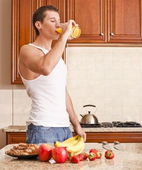 Young man wearing tank top and jeans in kitchen drinking a glass of orange juice. Vertical shot.