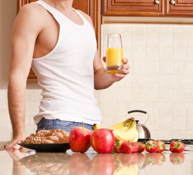 Young man wearing tank top and jeans in kitchen holding a glass of orange juice. Horizontal shot.