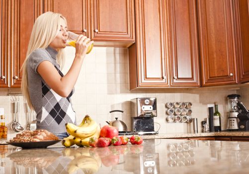 Young woman in kitchen drinking a glass of orange juice. Horizontal shot.