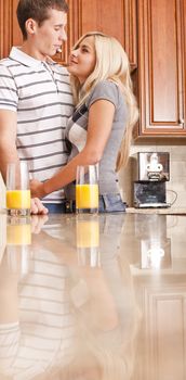 Young couple smiling at each other with glasses of orange juice on counter. Vertical shot.