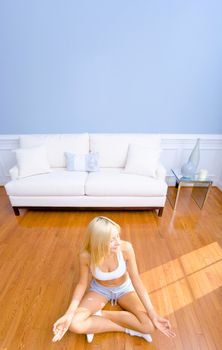 Young woman sitting cross legged on floor with hands on knees meditating. Vertical shot.