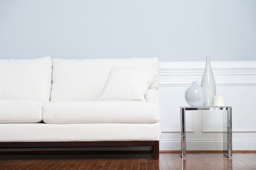 White sofa and glass end table with vases set against pale blue wall. Horizontal shot.