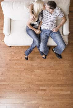 Young couple sitting on a cream colored love seat and kissing. Vertical shot