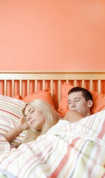 Young couple sleep closely together under a striped bedspread. Vertical shot.