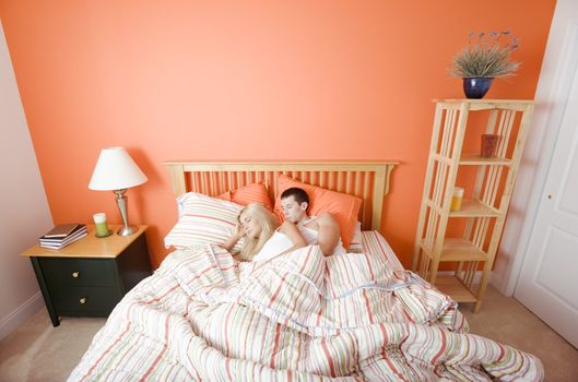 High angle view of young couple sleeping closely together under a striped bedspread. Horizontal shot.