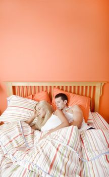 High angle view of young couple sleeping closely together under a striped bedspread. Vertical shot.