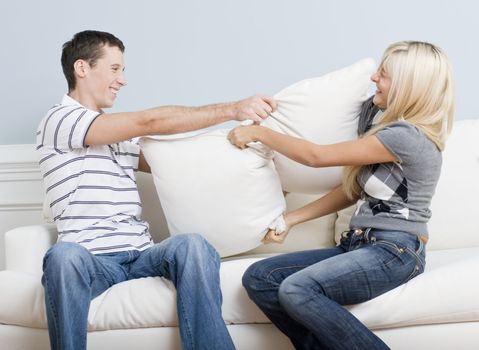 Young couple laugh while having a pillow fight on the sofa. Horizontal shot.