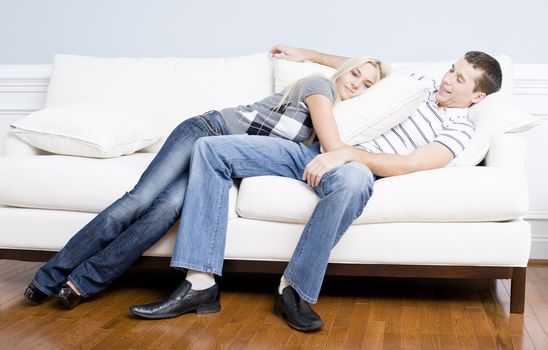 Young couple recline on a white sofa with the young woman lying on the man with a pillow. Horizontal shot.
