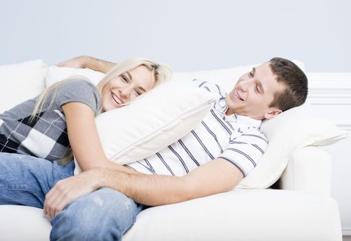 Young couple recline on a white sofa with the young woman lying on the man with a pillow. Horizontal shot.