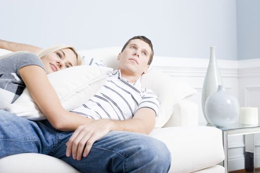 Woman snuggles up to man as they both relax quietly on a white couch. Horizontal format.