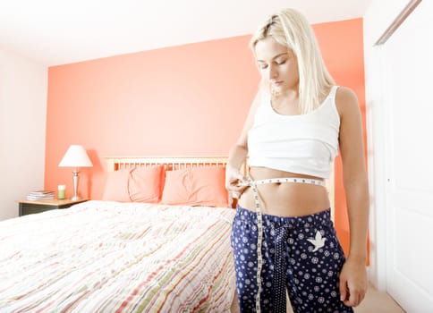 Woman standing in her bedroom and measuring her waist. Horizontal format.