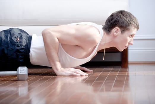 Cropped view of man doing push-ups next to couch. Horizontal format.