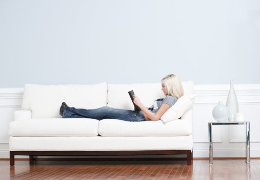 Full length view of woman reclining on white couch and reading a book. Horizontal format.