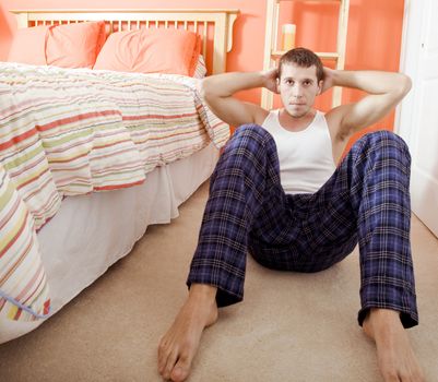 View of man facing the camera and doing sit-ups next to his bed. Horizontal format.