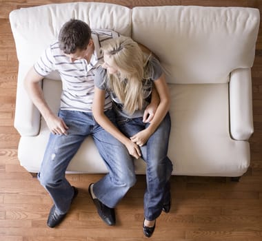 Full length overhead view of affectionate couple sitting together on white love seat. Square format.