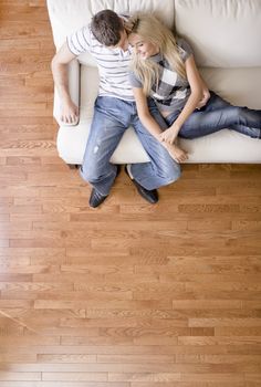 Cropped overhead view of affectionate couple sitting together on white love seat. Vertical format.