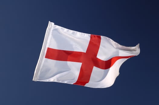 The cross of St George, the flag of England, isolated against a clear blue sky. Motion blur at the tip of the flag.